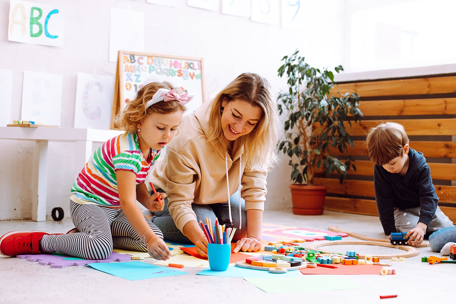 Kinder spielen mit bunten Bausteinen an einem Klassenzimmertisch, geleitet von einem lächelnden Lehrer in einer kreativen, inklusiven Lernumgebung.